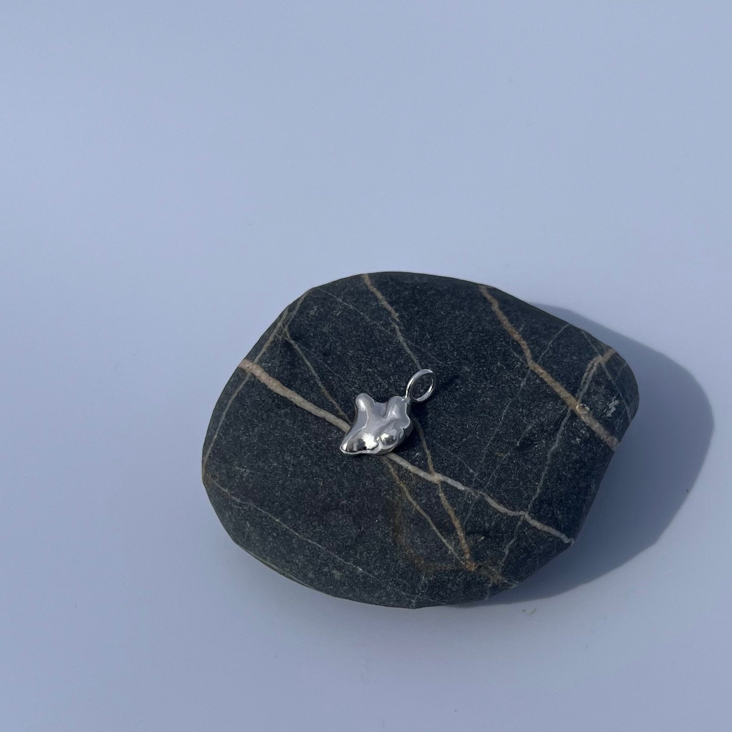 The swell pendant in sterling silver on a rock on a white background.