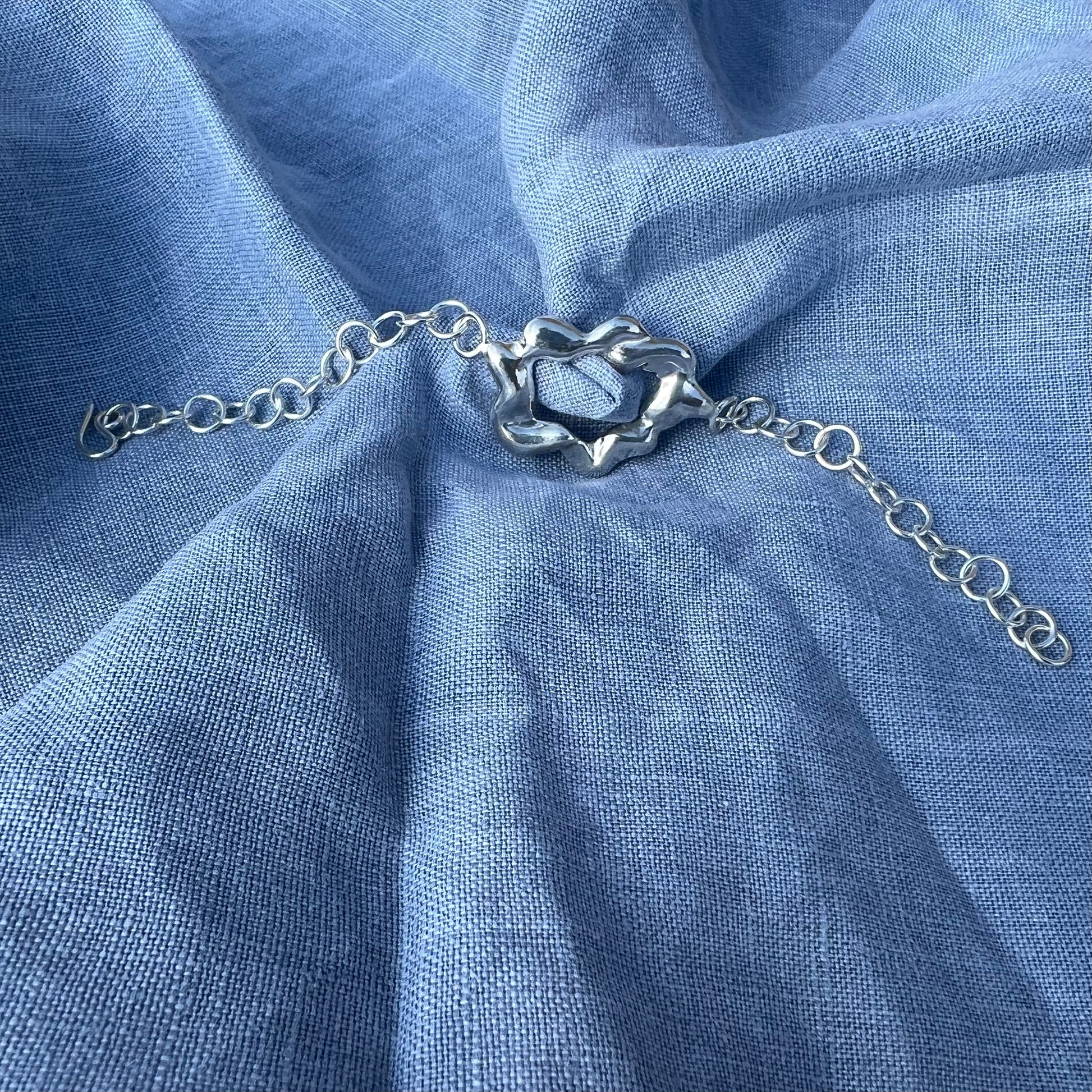 A chunky, statement handmade sterling silver bracelet on a blue linen background. The centrepiece of the bracelet is shaped like a cloud and it has a handmade hook clasp.