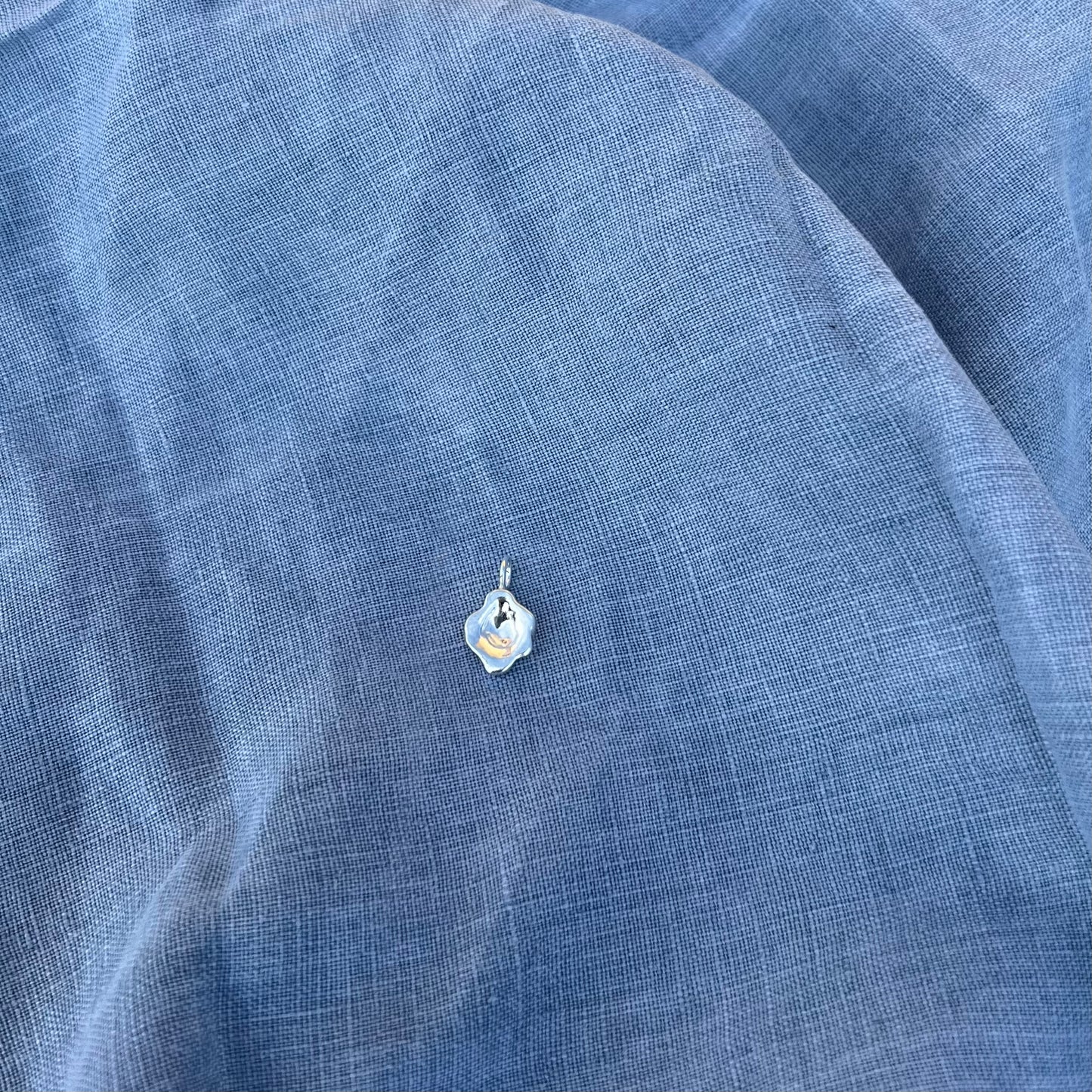 The swirl pendant from the back in sterling silver on a blue linen background.
