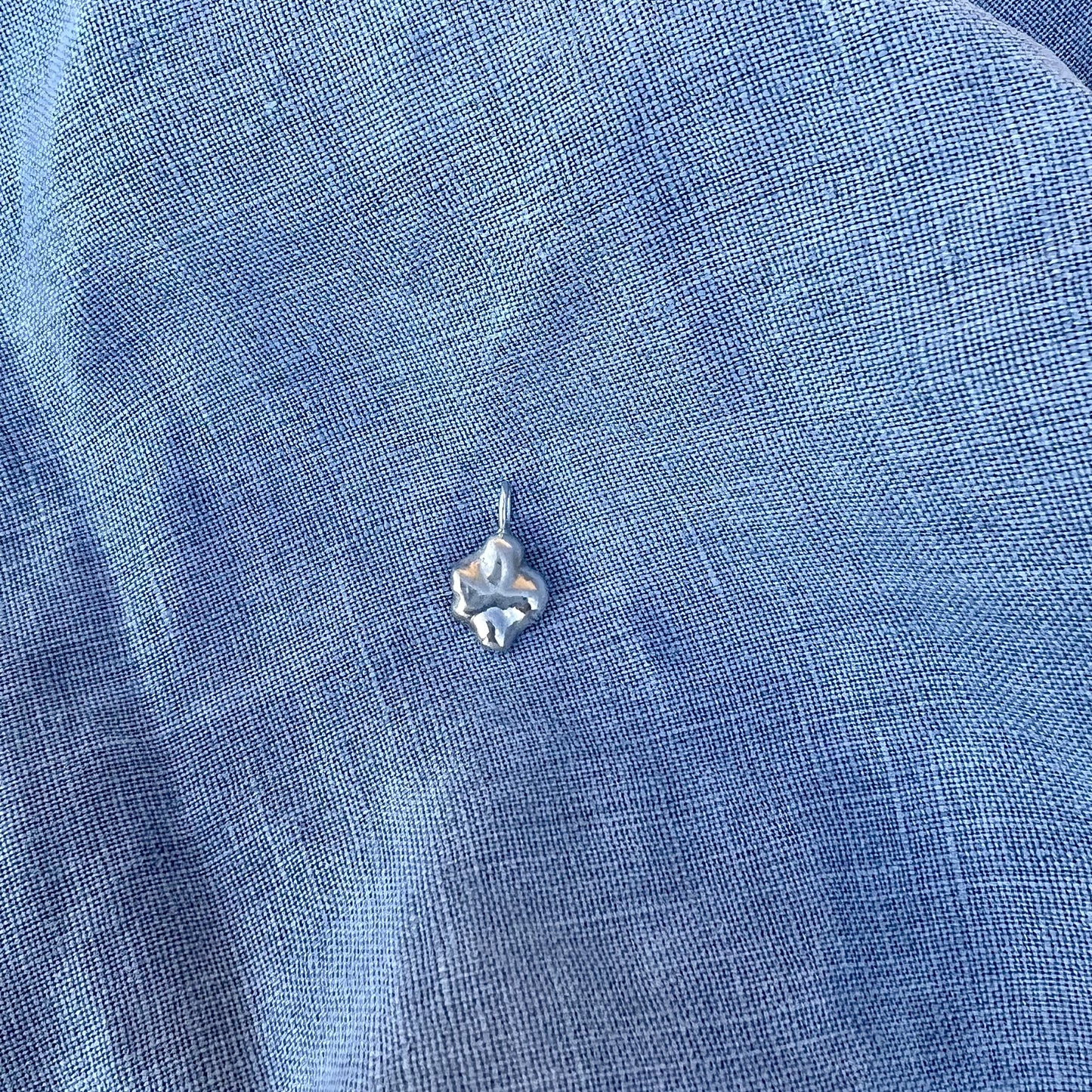 The sterling silver swirl pendant on a blue linen background.
