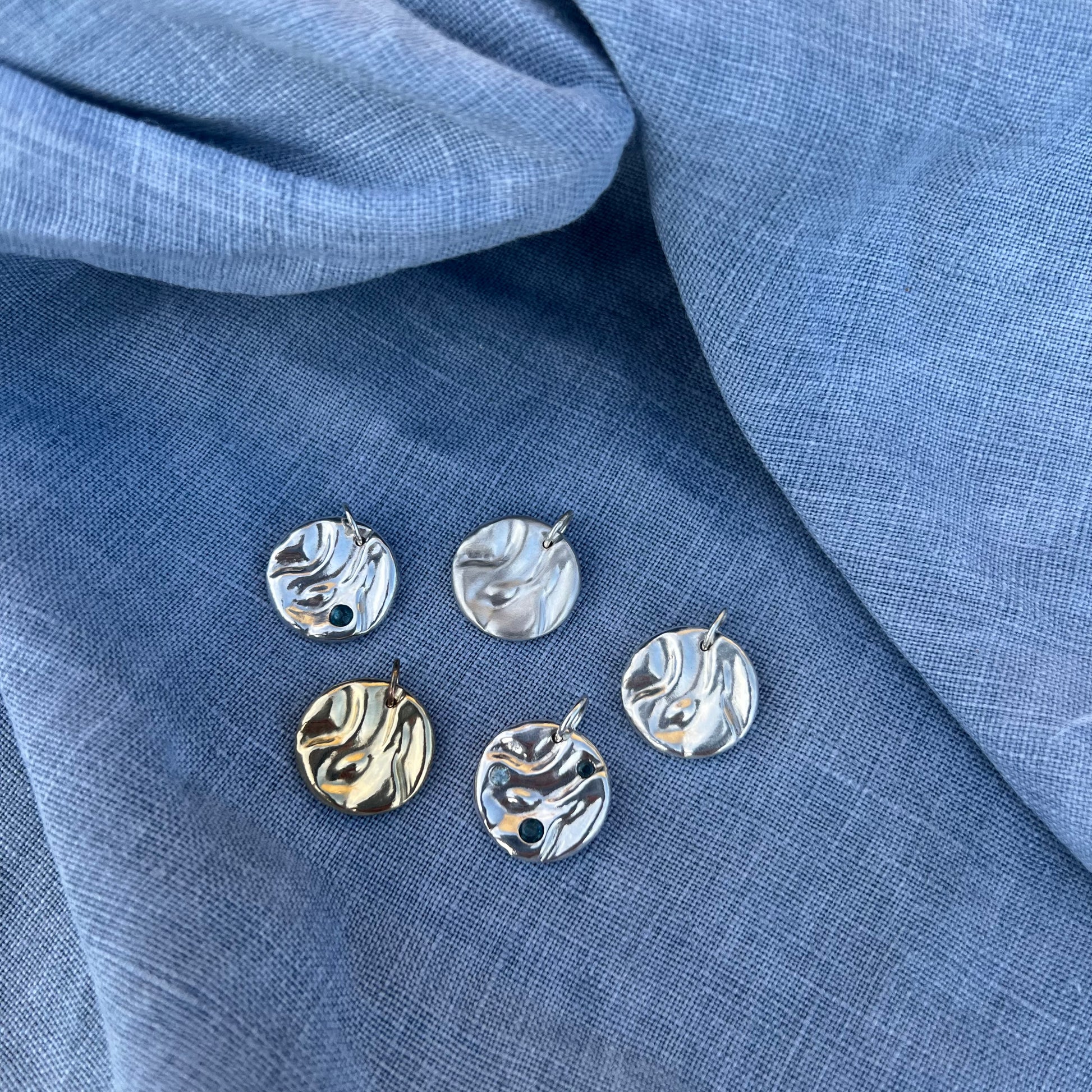 Five rock pool pendants - four sterling silver and one 9ct yellow gold pendant on a blue linen background.