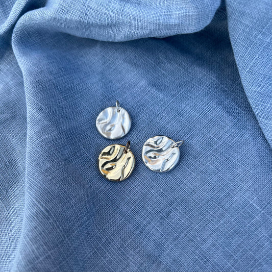 Two silver and one gold rock pool pendant on a blue linen background.