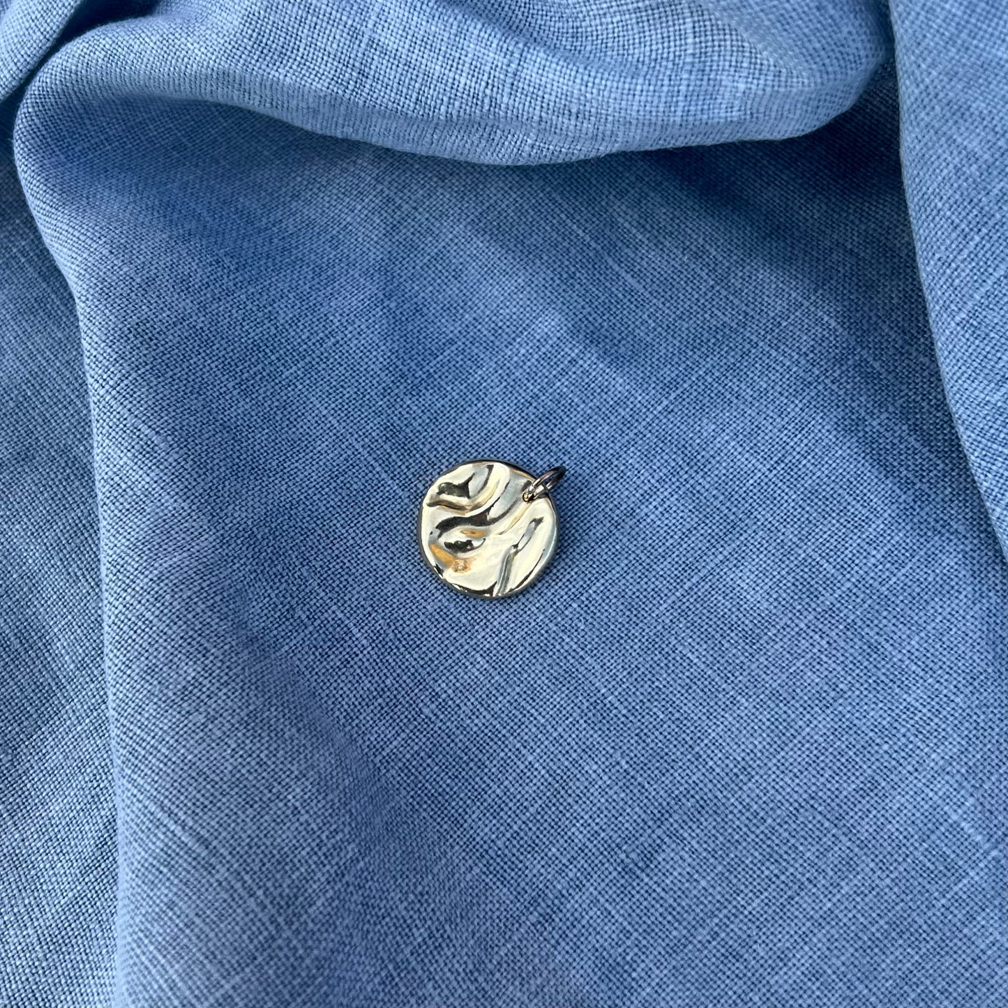 A rock pool pendant, handmade from recycled 9ct yellow goldon a background of blue linen.