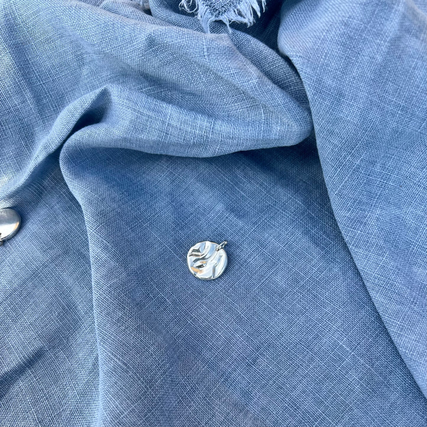 A shiny rock pool pendant, handmade from recycled silver on a background of blue linen.