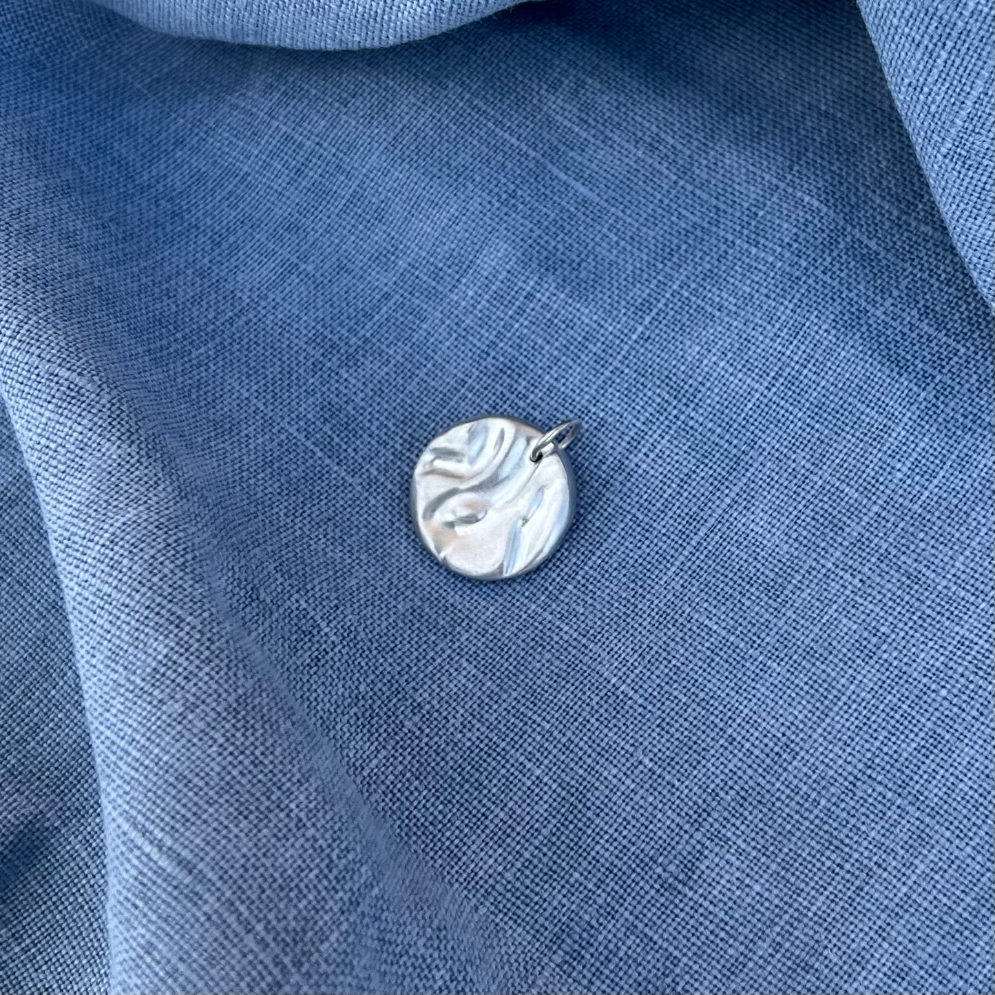 A matt rock pool pendant, handmade from recycled silver on a background of blue linen.