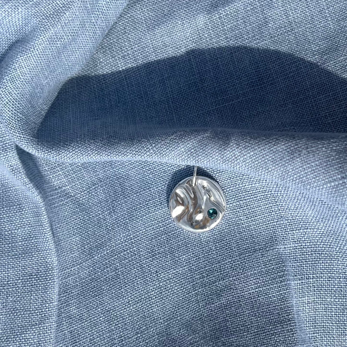 A topaz set rock pool pendant, handmade from recycled silver on a background of blue linen.