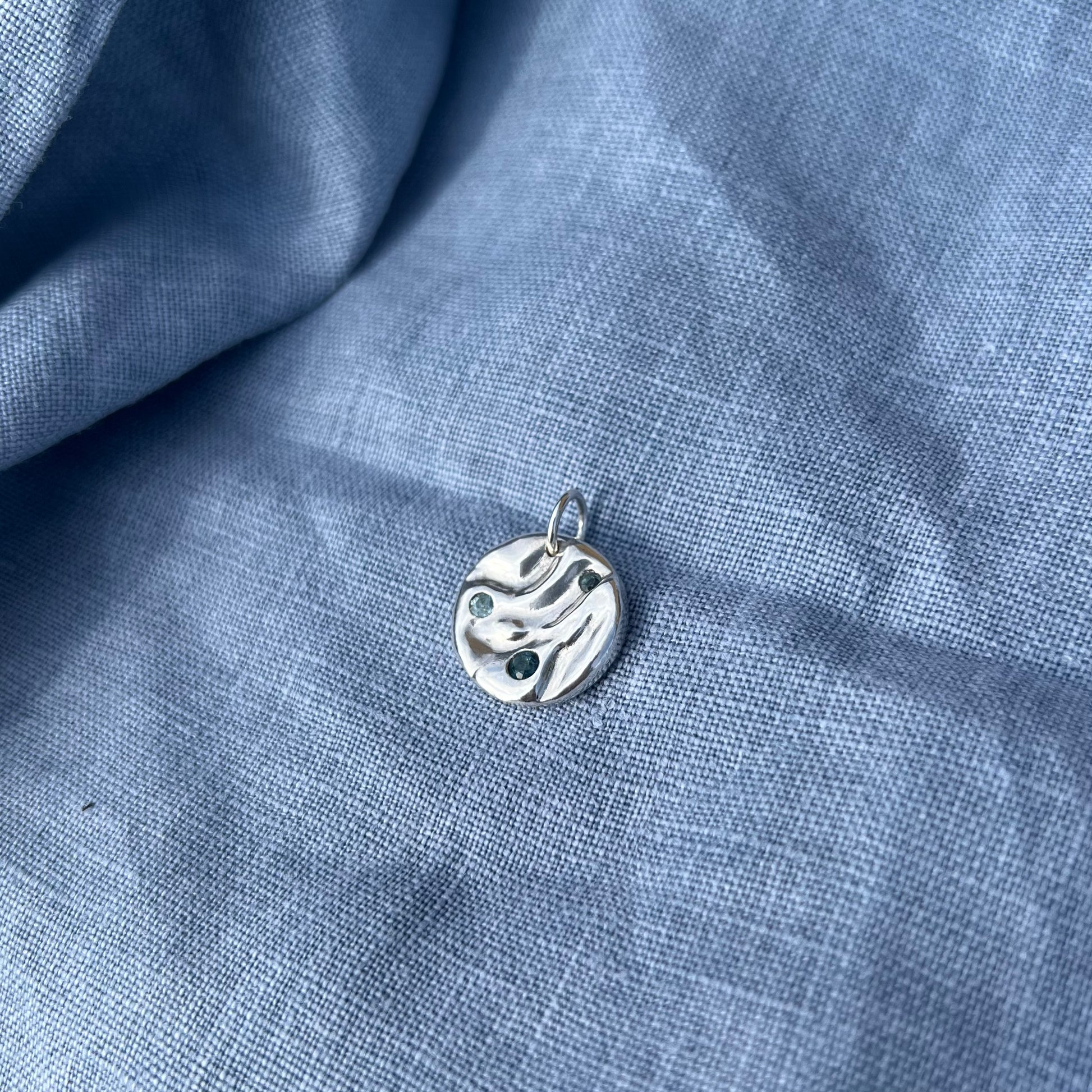 The triple topaz set rock pool pendant on a background of blue linen.
