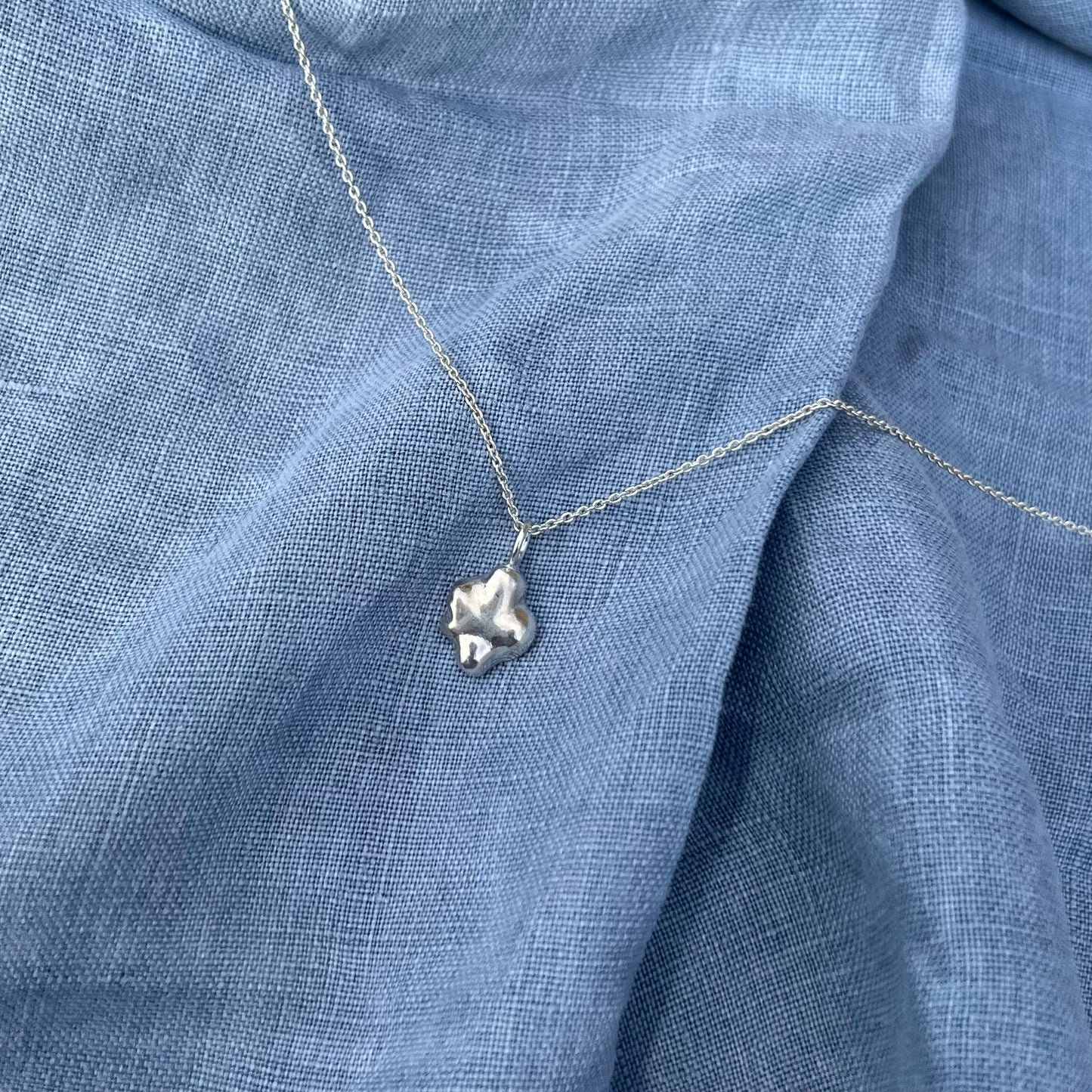 The swirl pendant in sterling silver on a chain with a blue linen background.