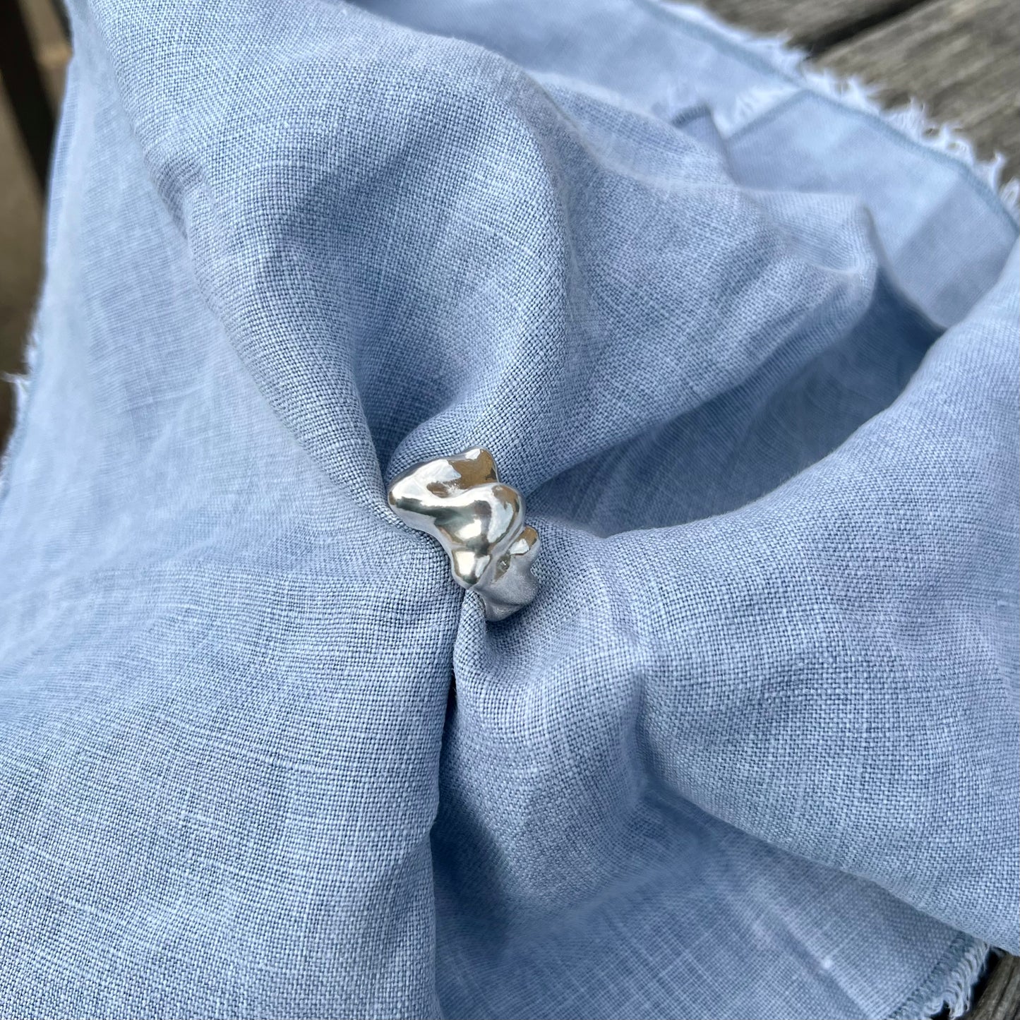 The Craggy ring. A chunky statement ring handmade in sterling silver which is photographed on a blue linen background. 