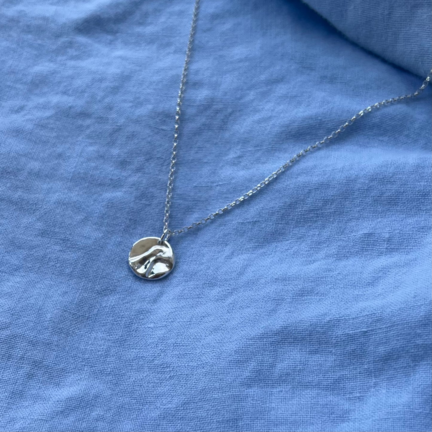 The sterling silver shiny pebble pendant on a chain on a blue background.