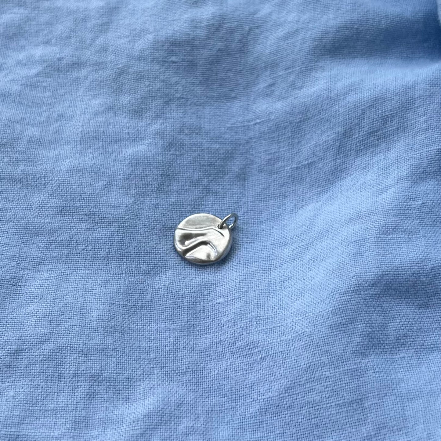 The sterling silver matt pebble pendant on a blue background.