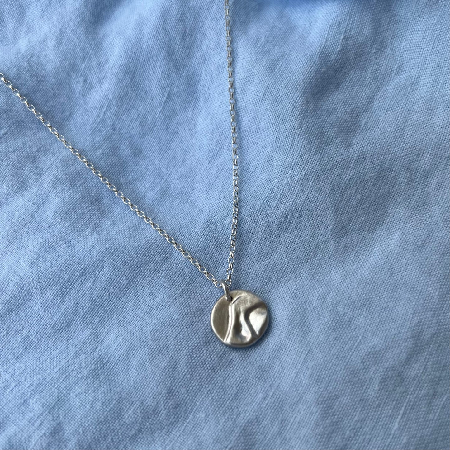 The sterling silver matt pebble pendant on a chain with a blue background.