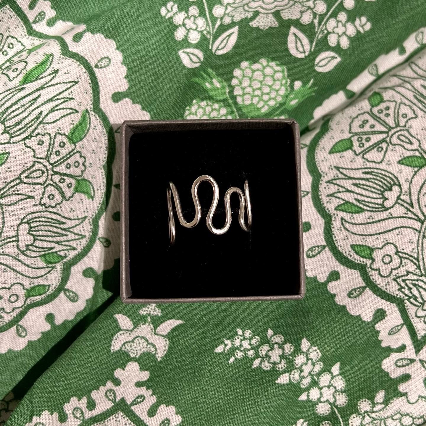 A sterling silver ripple ring on a green background.